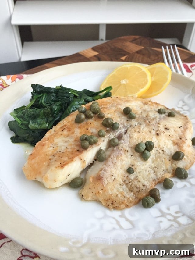 plate of white fish topped with capers with a side of cooked spinach and two lemon slices