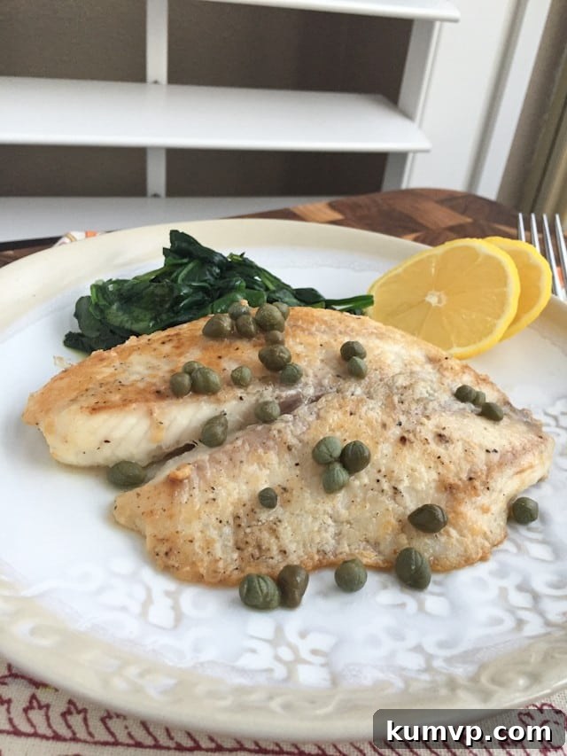 plate of white fish topped with capers with a side of cooked spinach and two lemon slices