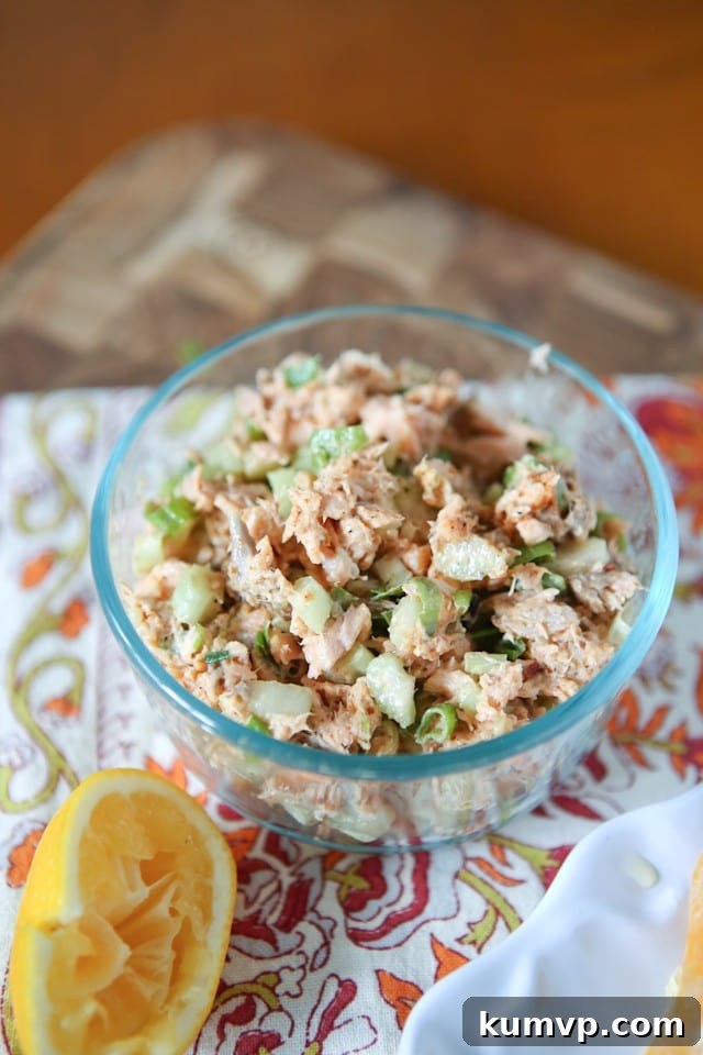 Blackened Salmon Salad A glass bowl filled with rich blackened salmon salad, placed on a woven placemat beside a freshly squeezed lemon half.