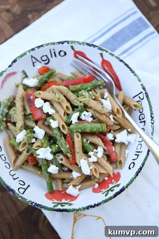 A vibrant bowl of Spring Vegetable Pasta with Pesto, featuring whole wheat pasta, fresh asparagus, red bell pepper, and peas in a light green pesto sauce.