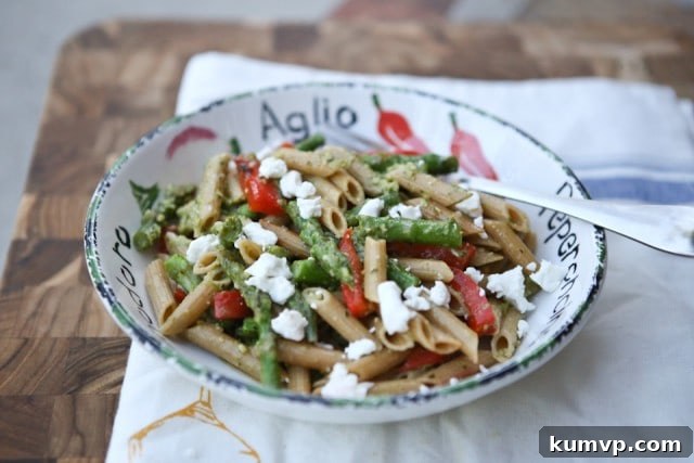 A close-up shot of Spring Vegetable Pasta with Pesto, showcasing the textures of whole wheat pasta, bright green asparagus, and diced red bell pepper.