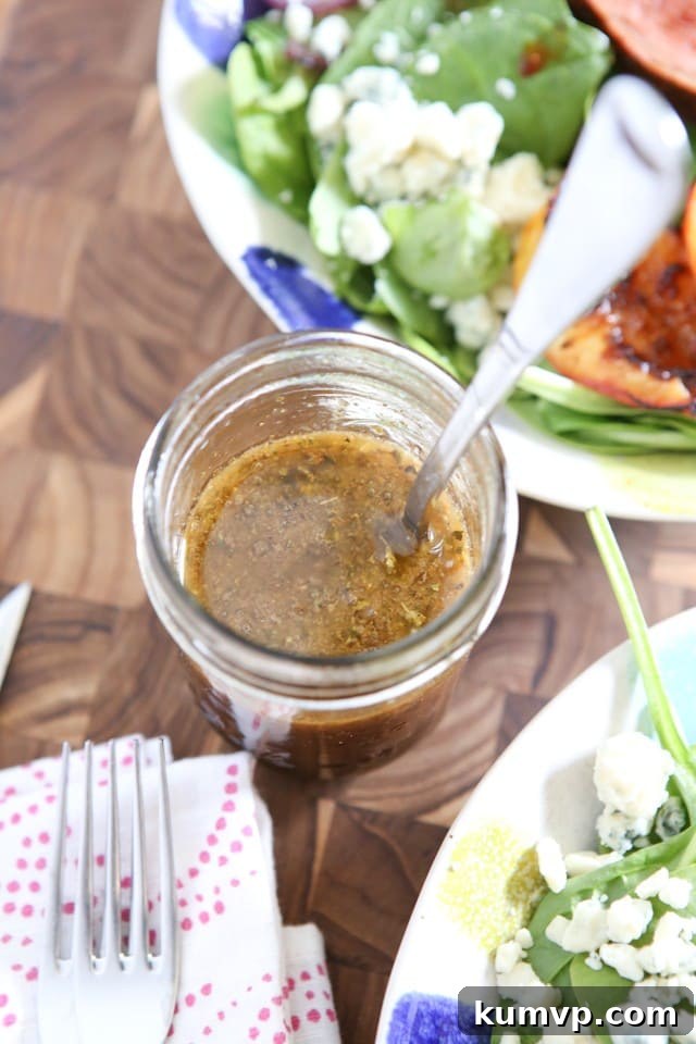 A close-up of a jelly jar brimming with homemade honey balsamic dressing, featuring fresh salad greens gently blurred in the background. The image emphasizes the ease and fresh flavor of making dressing at home.